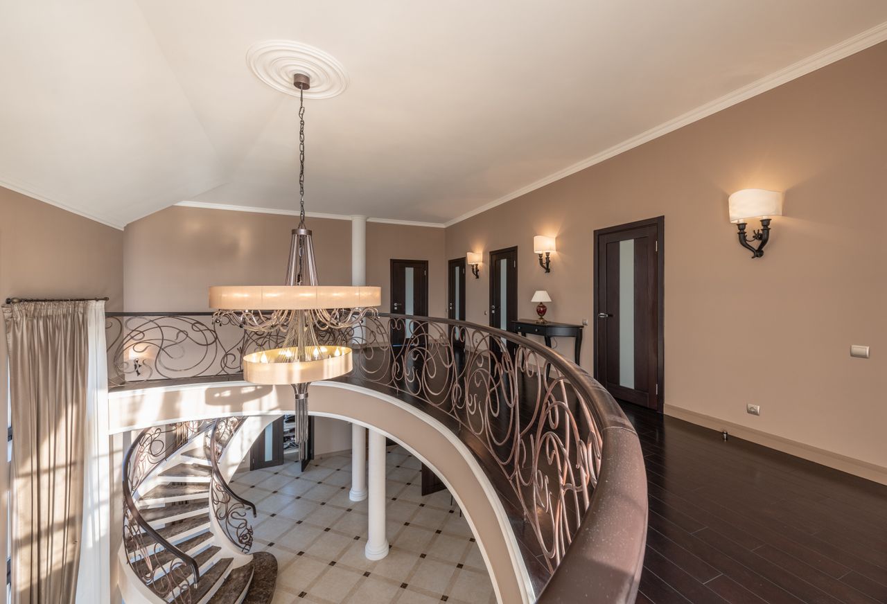Interior of modern spacious house with stairway and metal railings with decorative elements near wall with doors and glowing lamps